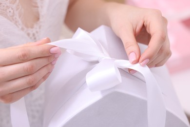 Photo of Bride opening beautiful wedding gift indoors, closeup