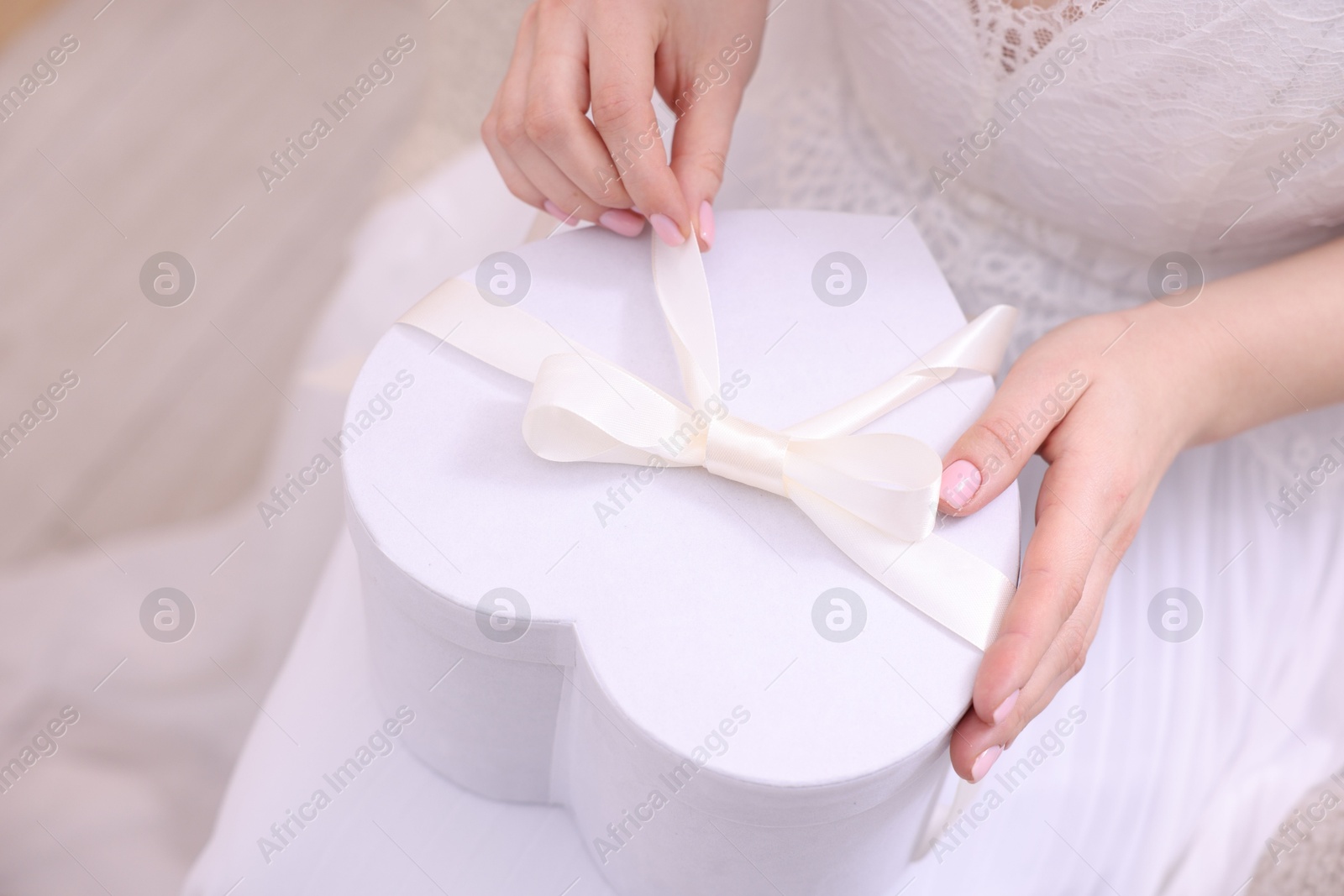 Photo of Bride opening beautiful wedding gift indoors, closeup