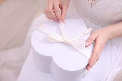 Photo of Bride opening beautiful wedding gift indoors, closeup