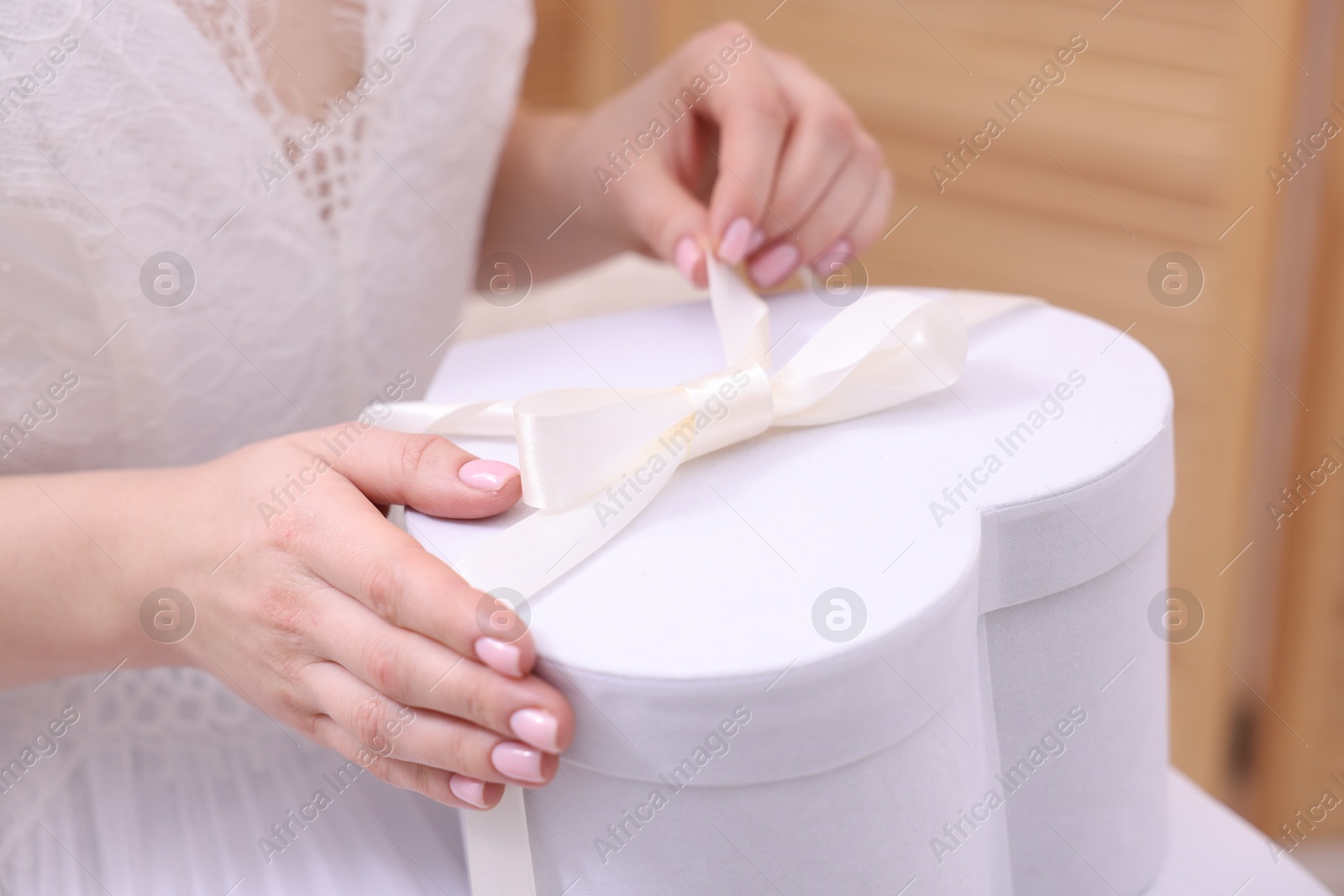 Photo of Bride opening beautiful wedding gift indoors, closeup