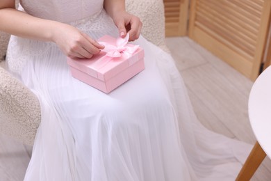 Photo of Bride opening beautiful wedding gift indoors, closeup