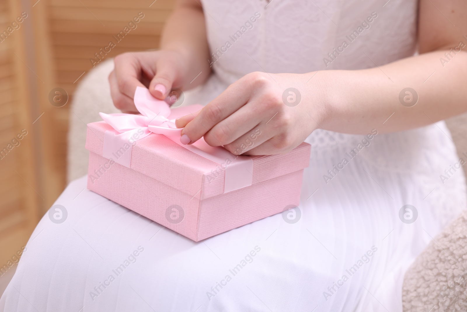 Photo of Bride opening beautiful wedding gift indoors, closeup