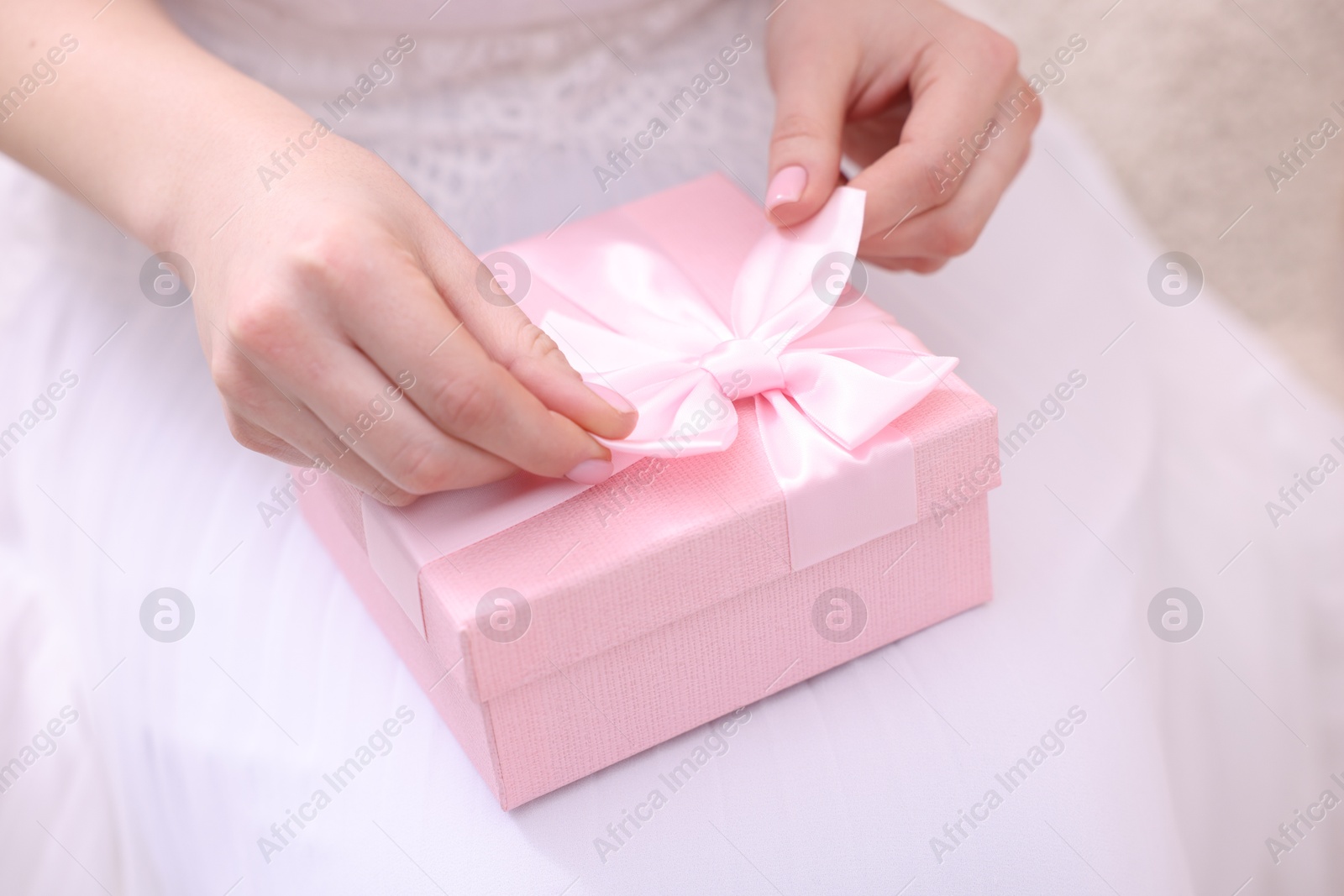 Photo of Bride opening beautiful wedding gift indoors, closeup