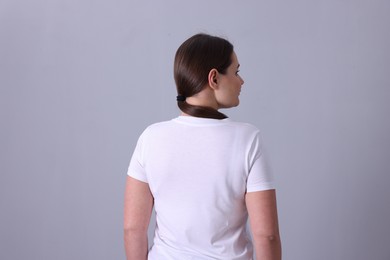 Photo of Woman in white t-shirt on grey background, back view. Mockup for design