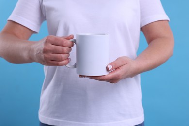 Photo of Woman with blank white cup on light blue background, closeup. Mockup for design