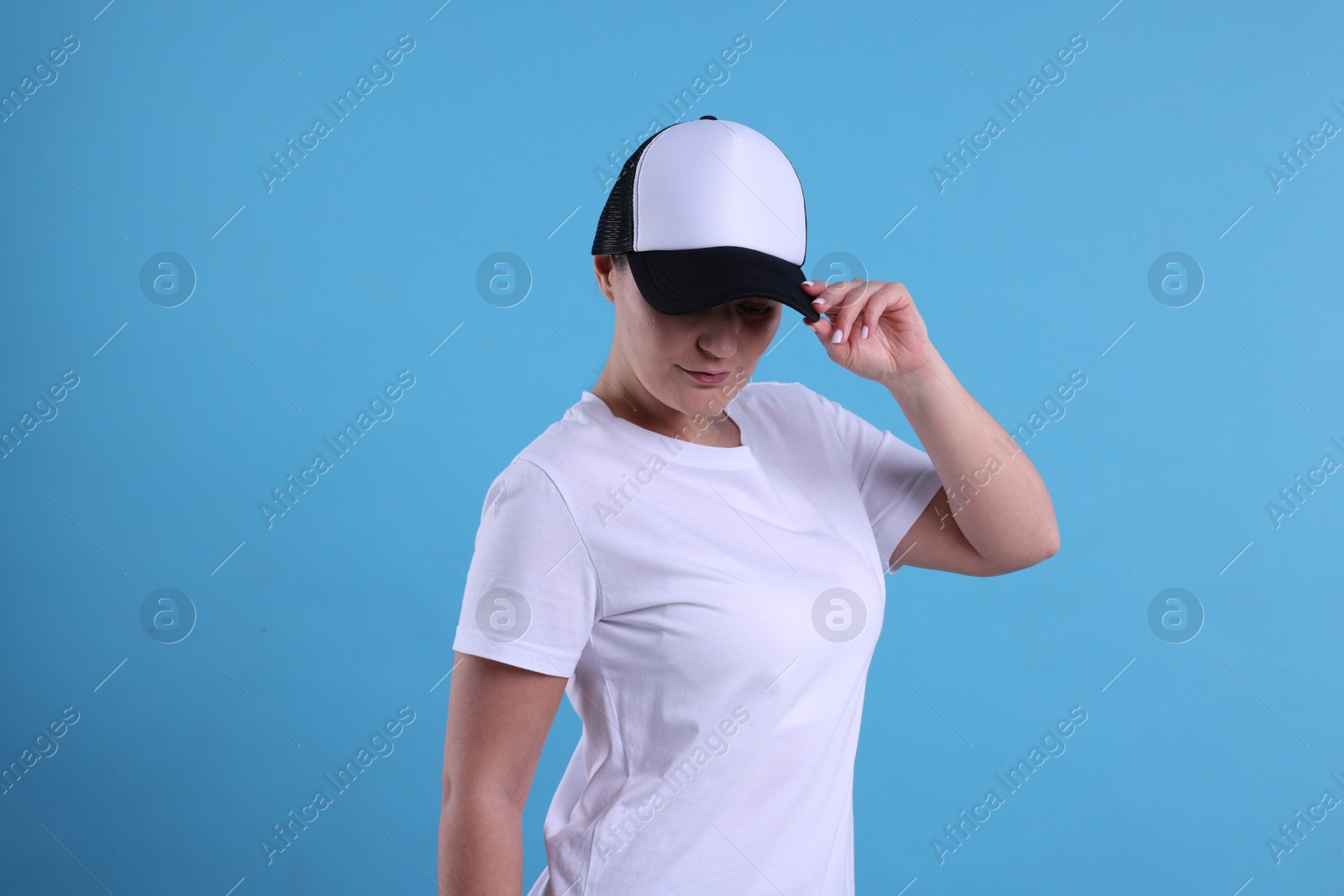 Photo of Woman in white t-shirt and baseball cap on light blue background. Mockup for design