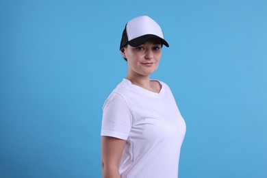 Photo of Woman in white t-shirt and baseball cap on light blue background. Mockup for design