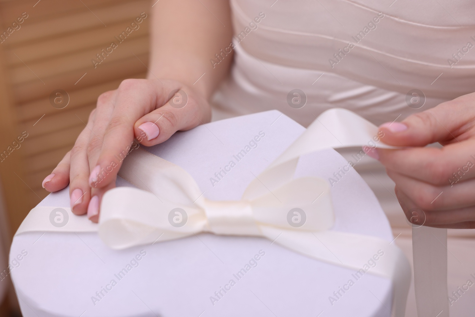 Photo of Bride opening beautiful wedding gift indoors, closeup