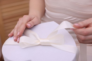 Photo of Bride opening beautiful wedding gift indoors, closeup