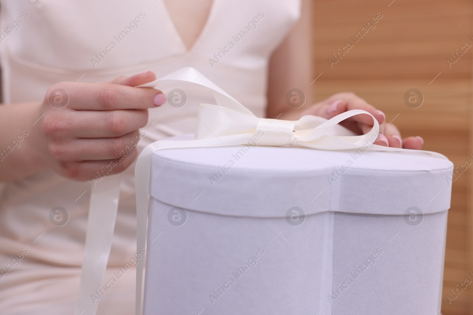 Photo of Bride opening beautiful wedding gift indoors, closeup