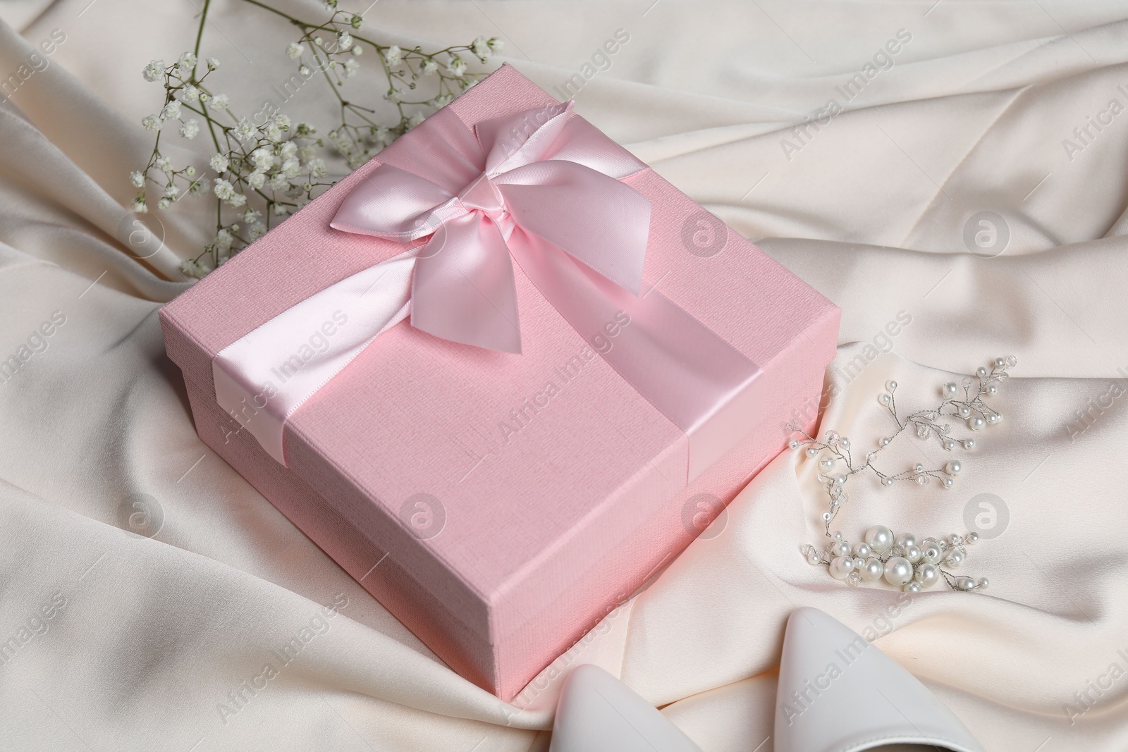 Photo of Beautiful wedding gift, pearl jewelry, bridal shoes and gypsophila flowers on beige silk fabric, closeup