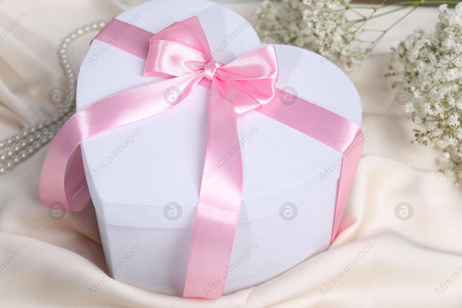 Photo of Beautiful wedding gift, pearl jewelry and gypsophila flowers on beige silk fabric, closeup