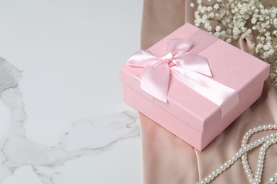 Photo of Beautiful wedding gift, pearl jewelry, silk fabric and gypsophila flowers on white marble table, space for text