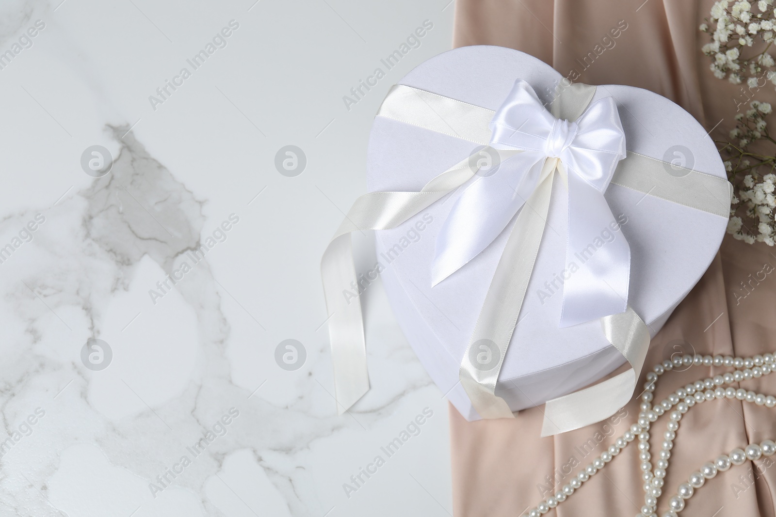 Photo of Beautiful wedding gift, pearl jewelry, silk fabric and gypsophila flowers on white marble table, above view. Space for text