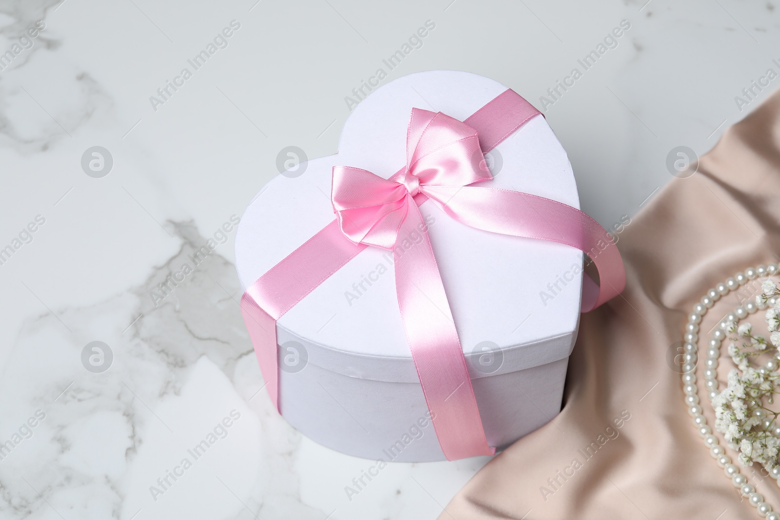 Photo of Beautiful wedding gift, pearl jewelry, silk fabric and gypsophila flowers on white marble table, space for text