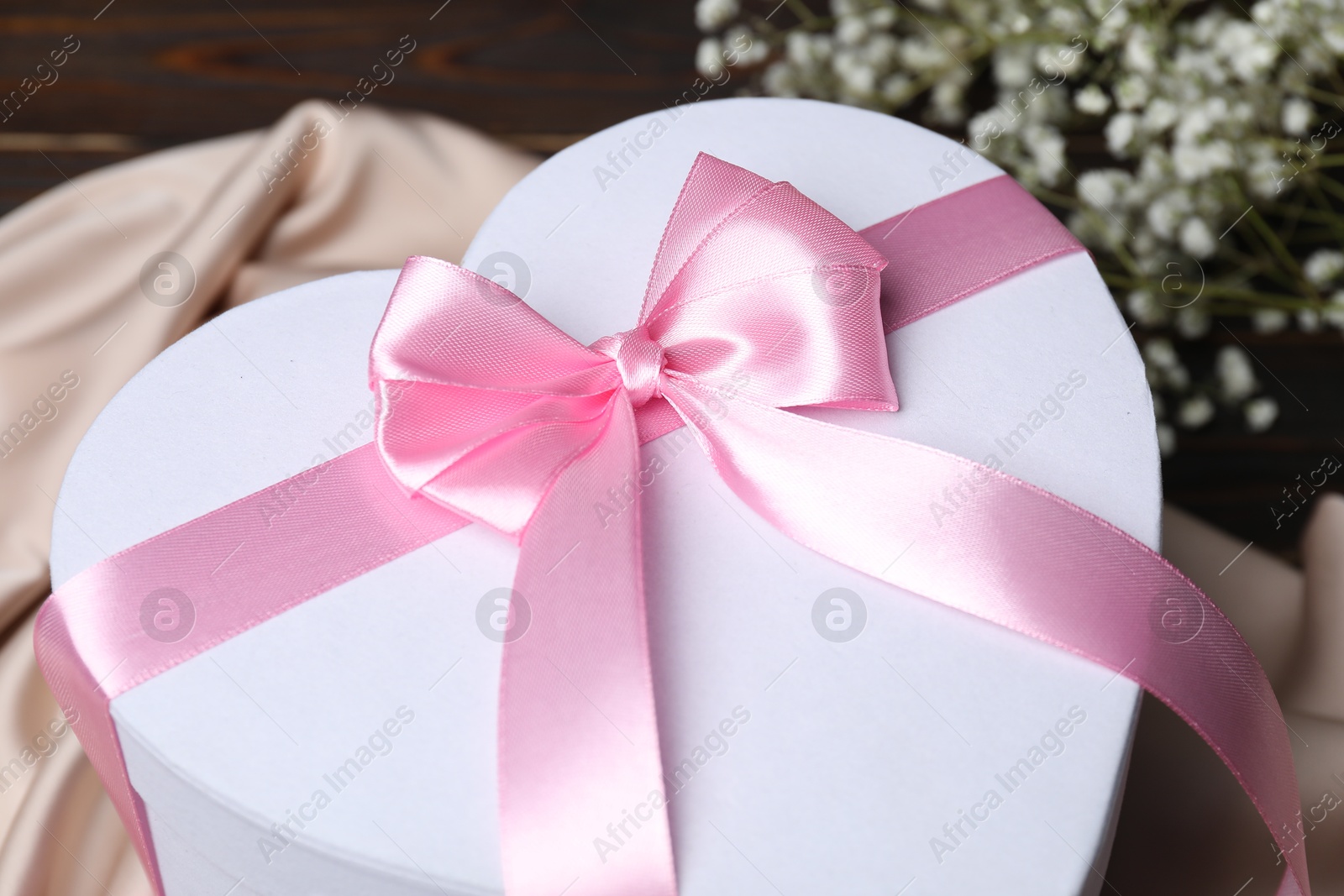 Photo of Beautiful wedding gift, silk fabric and gypsophila flowers on table, closeup