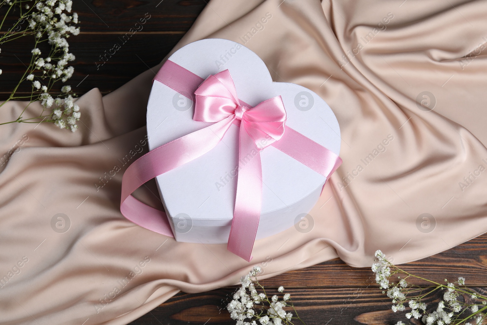 Photo of Beautiful wedding gift, silk fabric and gypsophila flowers on wooden table, above view