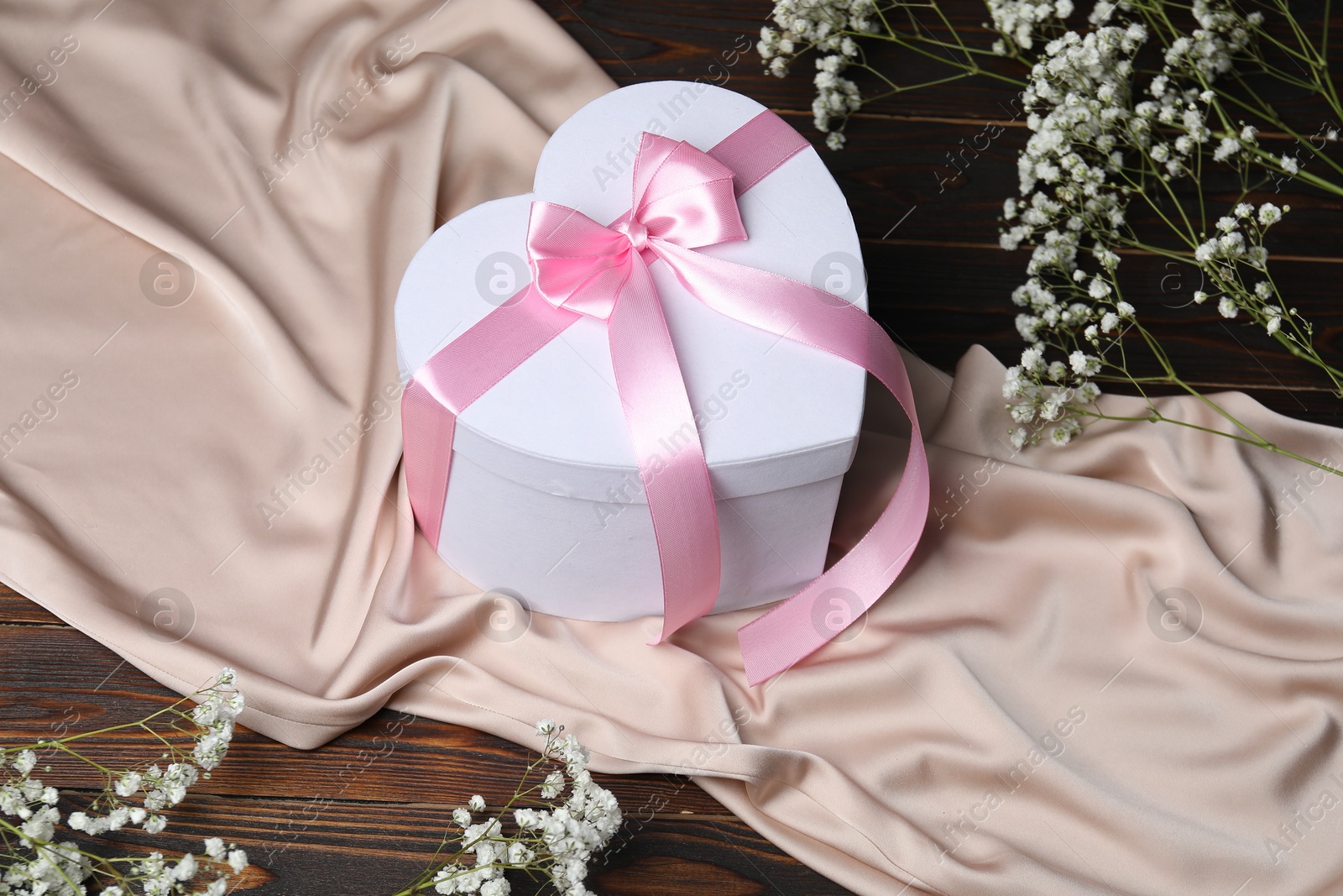 Photo of Beautiful wedding gift, silk fabric and gypsophila flowers on wooden table