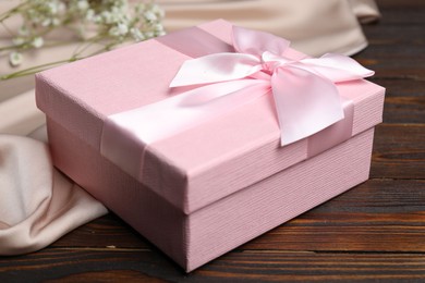 Photo of Beautiful wedding gift, silk fabric and gypsophila flowers on wooden table, closeup