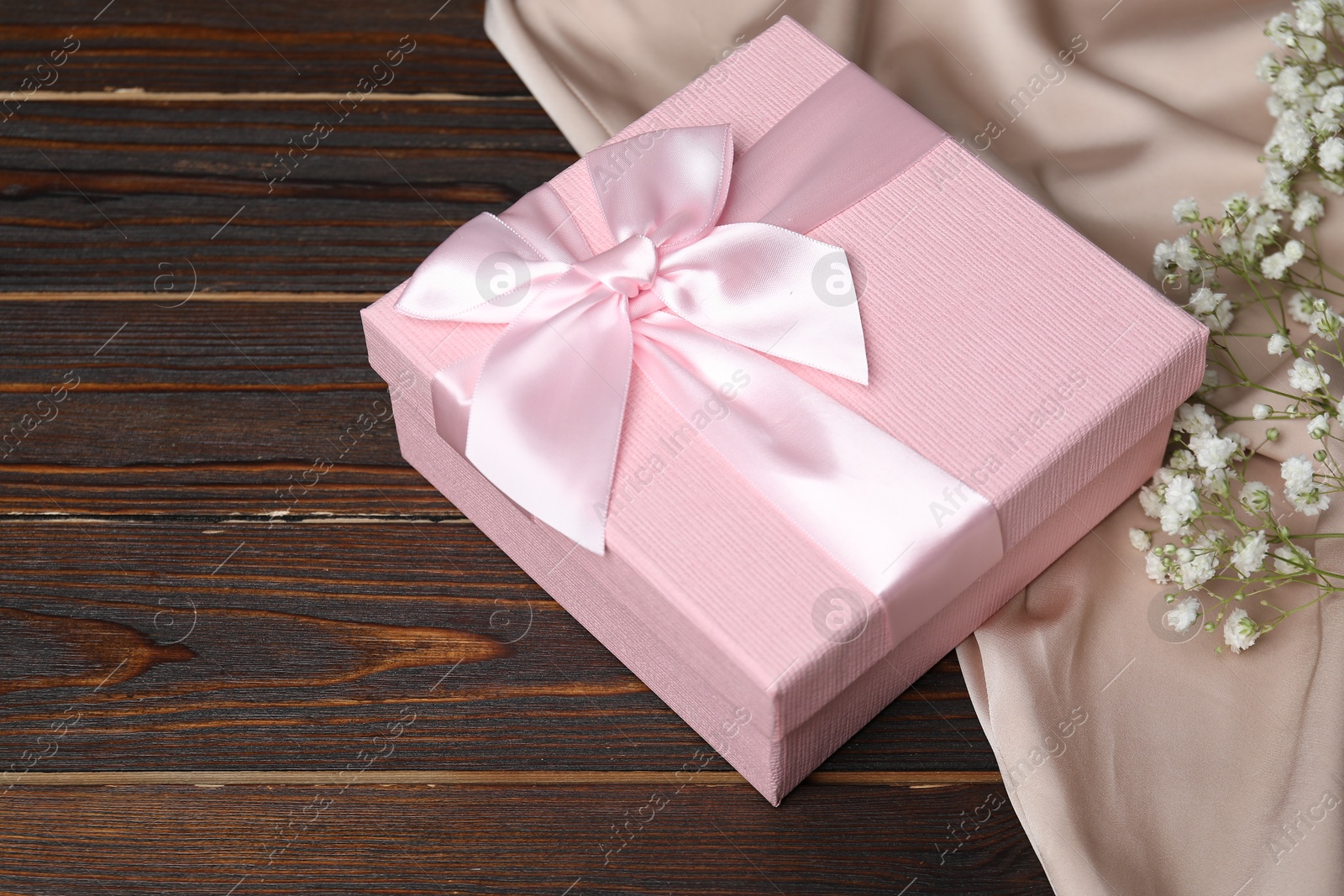 Photo of Beautiful wedding gift, silk fabric and gypsophila flowers on wooden table, closeup. Space for text