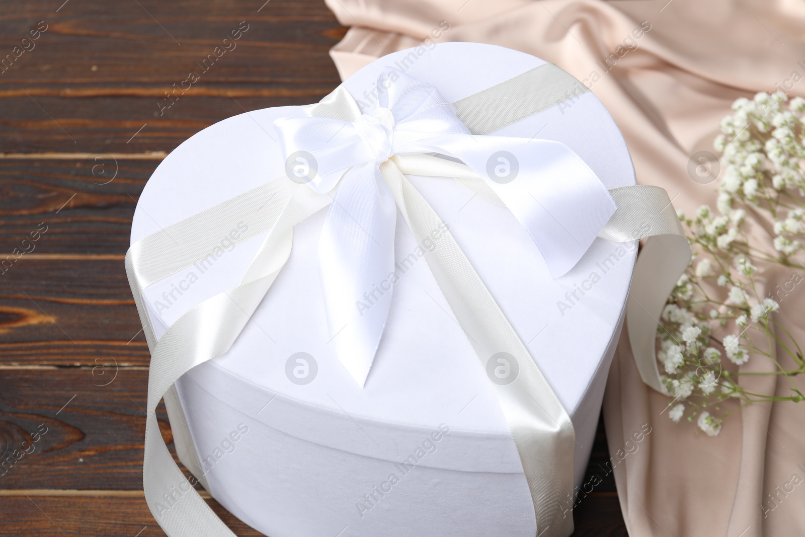 Photo of Beautiful wedding gift, silk fabric and gypsophila flowers on wooden table, closeup