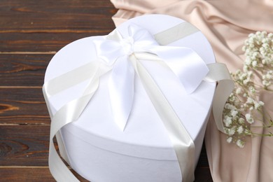 Photo of Beautiful wedding gift, silk fabric and gypsophila flowers on wooden table, closeup