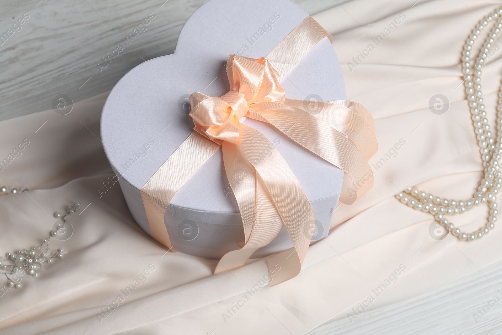 Photo of Beautiful wedding gift, pearl jewelry and silk fabric on light wooden table, above view