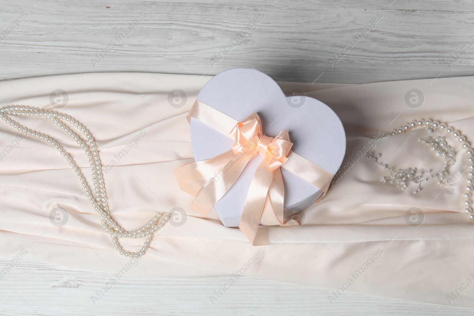 Photo of Beautiful wedding gift, pearl jewelry and silk fabric on light wooden table, flat lay