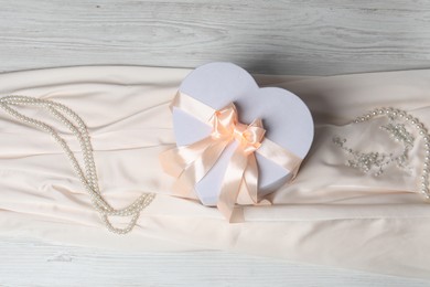 Photo of Beautiful wedding gift, pearl jewelry and silk fabric on light wooden table, flat lay