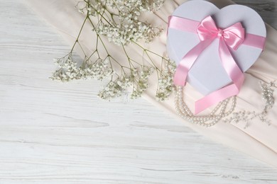 Photo of Beautiful wedding gift, pearl jewelry, silk fabric and gypsophila flowers on light wooden table, flat lay. Space for text