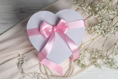 Photo of Beautiful wedding gift, pearl jewelry, silk fabric and gypsophila flowers on light wooden table, flat lay