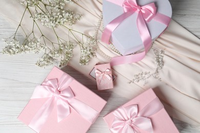 Photo of Beautiful wedding gifts, pearl jewelry, silk fabric and gypsophila flowers on light wooden table, flat lay