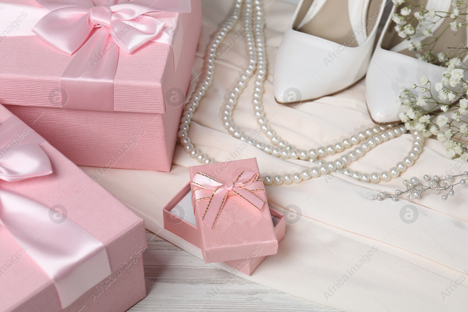 Photo of Beautiful wedding gifts, pearl jewelry, silk fabric, bridal shoes and gypsophila flowers on wooden table, closeup