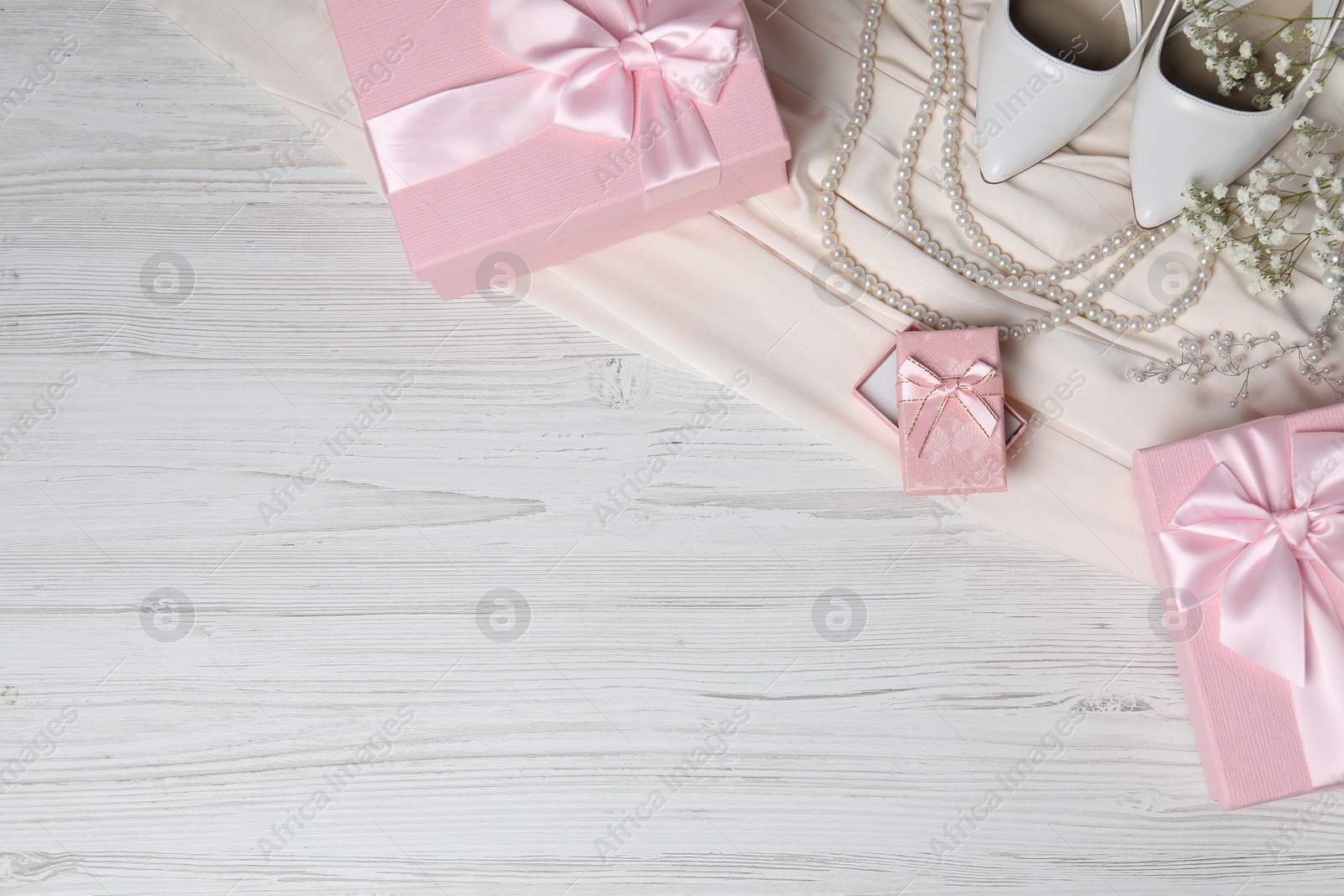 Photo of Beautiful wedding gifts, pearl jewelry, silk fabric, bridal shoes and gypsophila flowers on wooden table, flat lay. Space for text