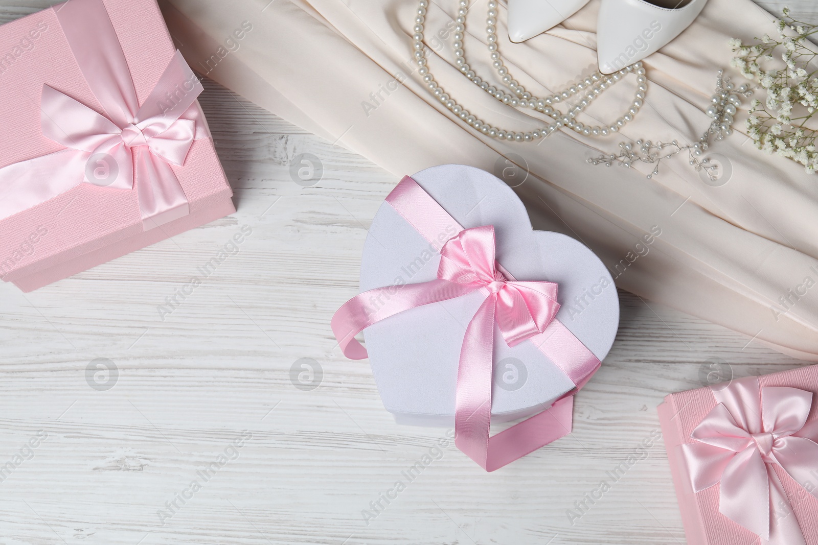 Photo of Beautiful wedding gifts, pearl jewelry, silk fabric, bridal shoes and gypsophila flowers on wooden table, flat lay. Space for text