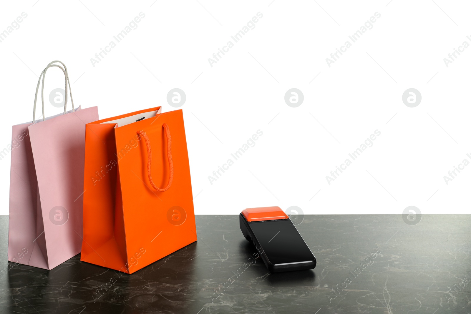 Photo of Payment terminal and shopping bags on dark marble table against white background