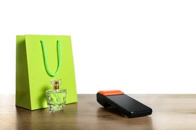 Photo of Payment terminal, perfume and shopping bag on wooden table against white background