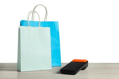 Photo of Payment terminal and shopping bags on wooden table against white background