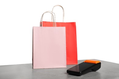 Photo of Payment terminal and shopping bags on grey table against white background