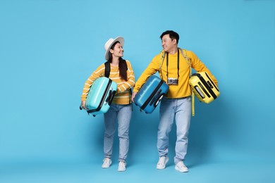 Photo of Happy travellers carrying suitcases on light blue background