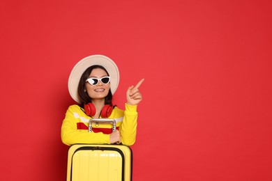 Photo of Happy traveller with suitcase pointing at something on red background. Space for text