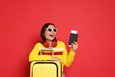 Photo of Happy traveller with headphones, passport and suitcase on red background