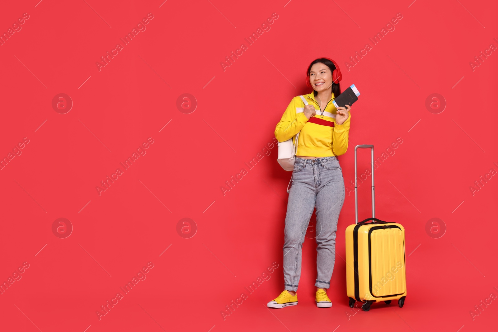 Photo of Happy traveller with passport and suitcase on red background. Space for text