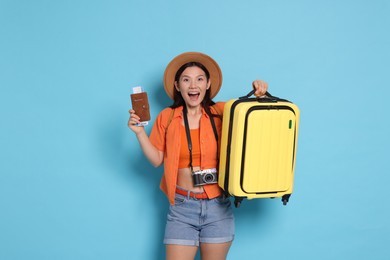 Photo of Excited traveller with passport and suitcase on light blue background