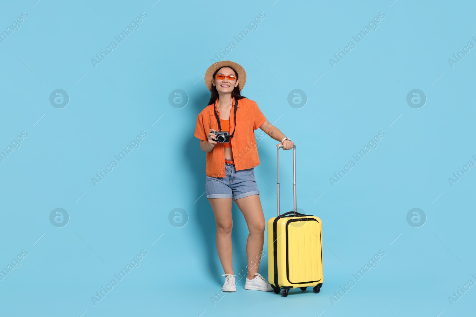 Photo of Happy traveller with camera and suitcase on light blue background