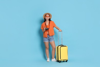 Photo of Happy traveller with camera and suitcase on light blue background