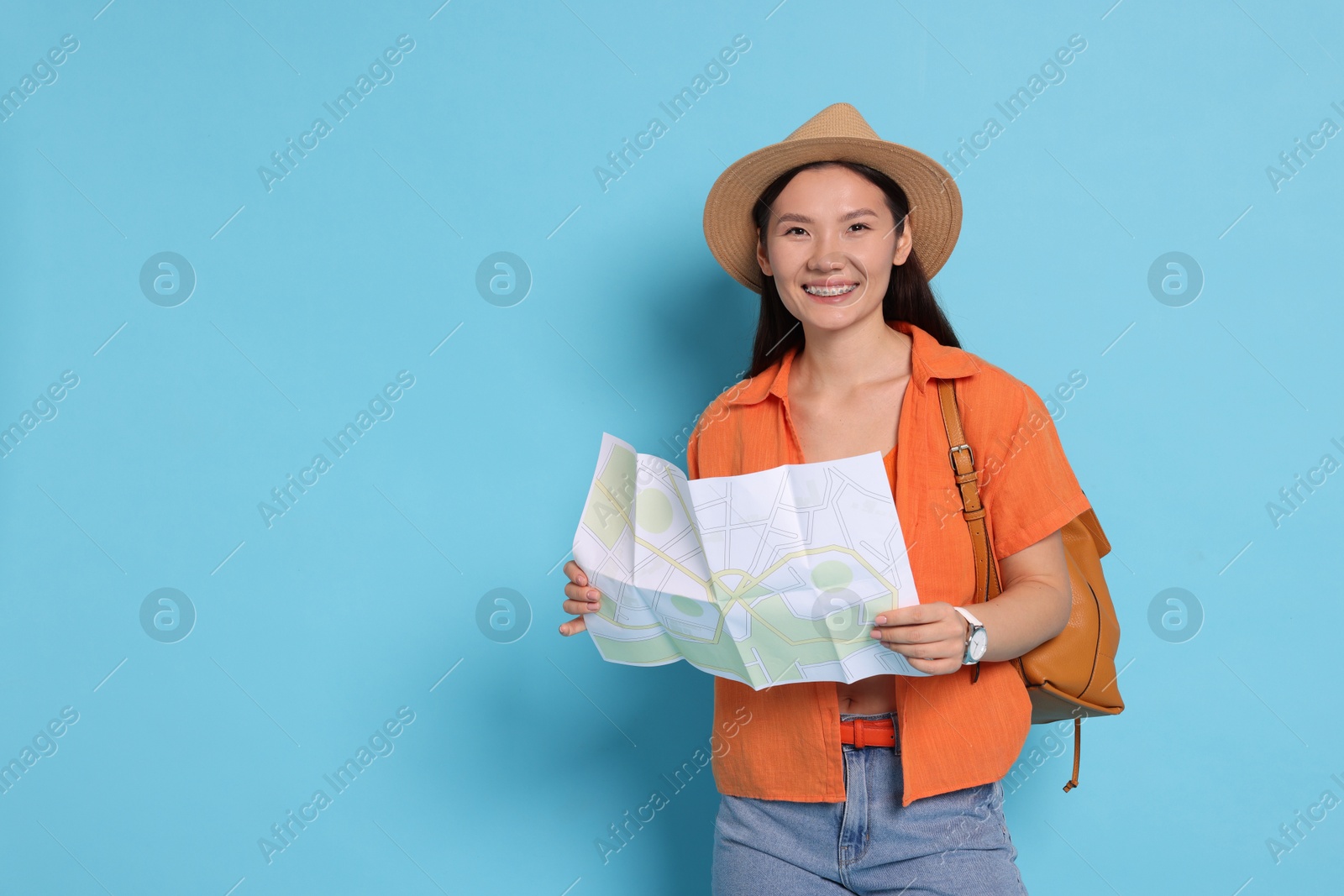 Photo of Happy traveller with backpack and map on light blue background. Space for text