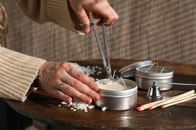 Photo of Woman cutting soy candle wick with trimmer at wooden table, closeup