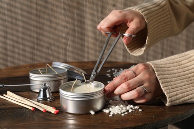 Photo of Woman cutting soy candle wick with trimmer at wooden table, closeup