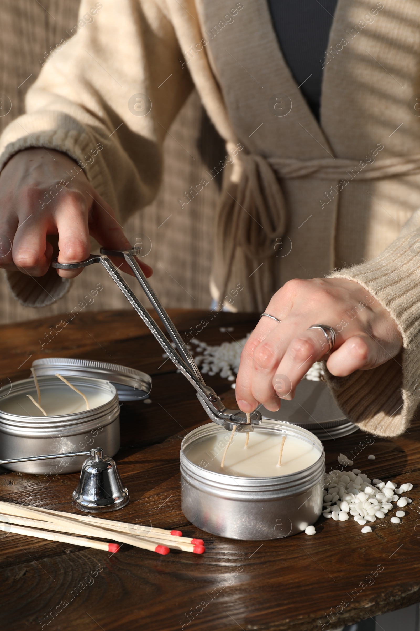 Photo of Woman cutting soy candle wick with trimmer at wooden table, closeup